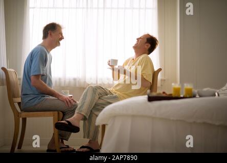 Coppia omosessuale maschio ridere insieme mentre si siede nella loro camera da letto. Foto Stock
