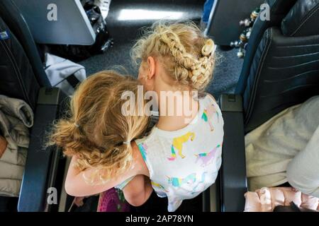 sorelle che camminano attraverso la navata dell'aeroplano verso il hugging del sedile Foto Stock