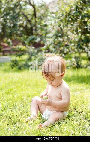 Il ragazzino si sietta sull'erba e tiene una mela Foto Stock