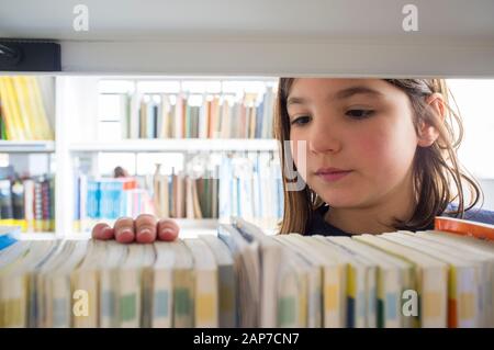 Ragazza giovane selezione di libri dalla biblioteca scaffale. I bambini la creatività e la fantasia del concetto. Foto Stock