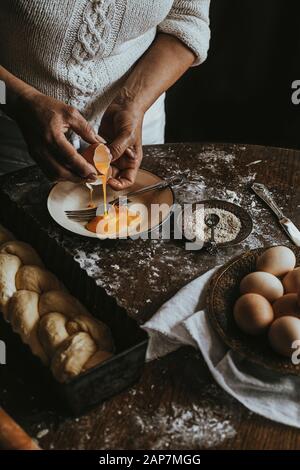 Una donna si prepara in casa pane intrecciato a casa. Close up della donna le mani e schizzi di uovo Foto Stock