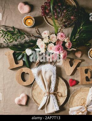 St. Il giorno di San Valentino o di un matrimonio romantico impostazione tabella con lettere in legno amore, ago cuori feltrato, bouquet di rose rosa e uve rosse sul naturale l Foto Stock