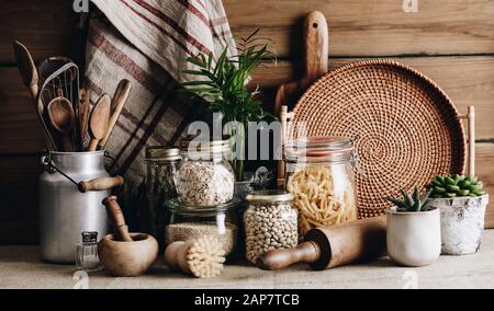 Cucina eco-friendly concetto: Utensili da cucina, piante da casa e cucina ingredienti in vasi di vetro contro parete cucina rustica, vista frontale Foto Stock