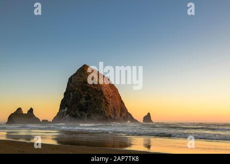 Haystack Rock situato a Cannon Beach, Oregon al tramonto con Orange e Blue Skies. Foto Stock