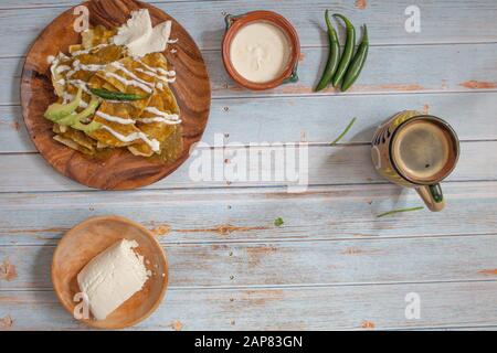 presentazione di cibo messicano con chilaquiles in salsa verde, caffè messicano in tazza folclorica con formaggio, panna e peperoncino su tabl di legno blu Foto Stock