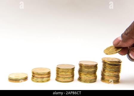 Monete canadesi in dollari saccheggiate in cinque pile ascendenti su sfondo bianco. Mano può essere visto prendere o aggiungere una moneta al palo. Foto Stock
