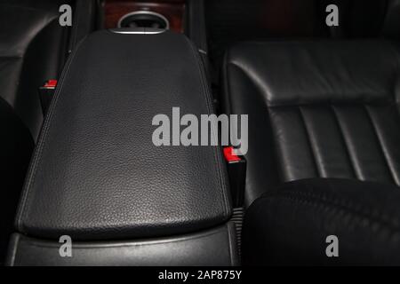 Primo piano sul bracciolo anteriore dell'auto con finiture in pelle nera, pulsanti e cinture di sicurezza all'interno dopo la pulizia a secco e dei dettagli. Indust. Autom Foto Stock