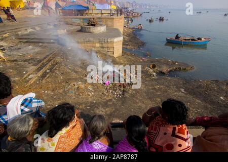Le donne guardano sulla riva del fiume Gange come una pirre funeraria brucia giù. A Varanasi, Benares, Uttar Pradesh, India. Foto Stock