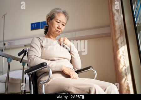 triste e depressa donna asiatica anziana seduta da sola in sedia a rotelle con testa giù in casa di cura Foto Stock