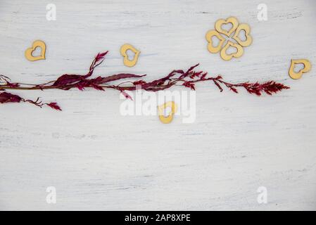 Un ramo rosso asciutto e cuori di legno su uno sfondo chiaro. Foto Stock