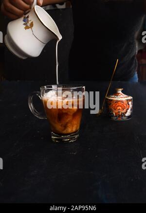 Mano di donna che versava il latte nel caffè, con il vaso di zucchero sullo sfondo. Stile loft Instagram pour shot. Latte di mandorle versato nel caffè vegano, Foto Stock