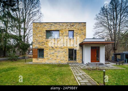 Un esterno di facciata di una moderna casa privata a due piani. Porta d'ingresso. Muro di mattoni gialli. Parete bianca. Vista frontale. Foto Stock