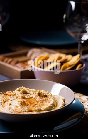 Gustoso hummus ceci salsa alimentare su un piatto su un tavolo da pranzo con tessuti blu e grigi su sfondo nero Foto Stock