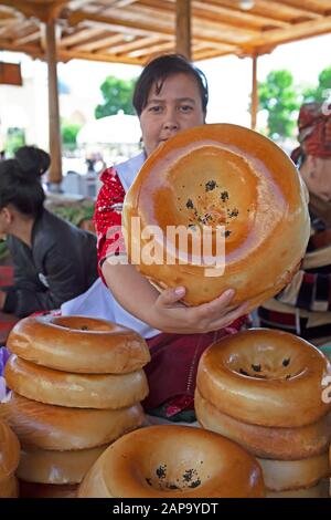 Donna mostra un pane Samarcanda tradizionale, il bazar Siyob Samarcanda, la provincia di Samarqand, Uzbekistan Foto Stock