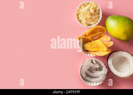 Disidratato ed essiccato di mango e scaglie di noce di cocco nella ciotola bianco su sfondo rosa. Vista da sopra. Foto Stock