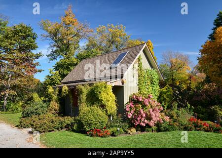 Grazioso cottage fiorito coperto di vegetazione lussureggiante e solare-alimentato da pannelli sul suo tetto, un modello di sviluppo sostenibile Foto Stock