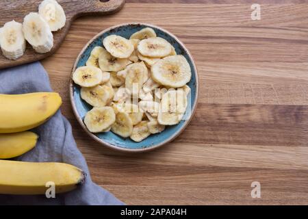 Trucioli di banana disidratati, freschi e secchi in ciotola su tagliere. Vista dall'alto. Foto Stock