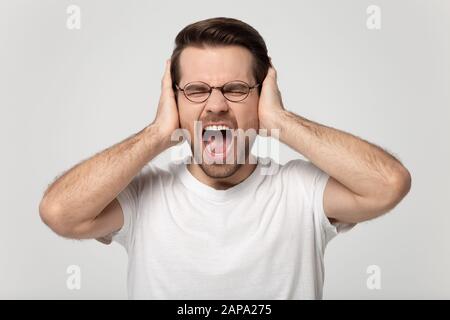 Primo piano ritratto headshot giovane stressato uomo che copre le orecchie. Foto Stock