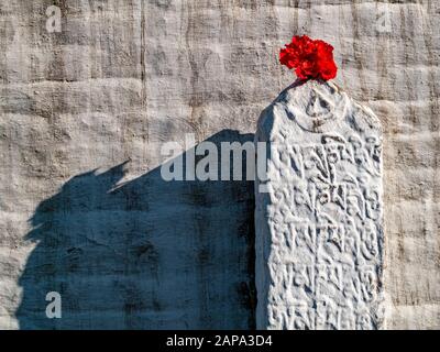 Fiore rosso come offerta su una roccia con scritta tibetana incisa a Boudha Stupa Foto Stock