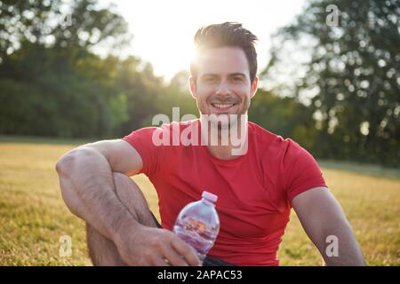 Uomo sorridente che riposa dopo l'allenamento all'aria fresca Foto Stock