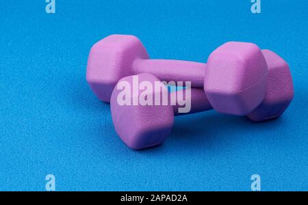 un paio di dumbbell viola in plastica per un tappetino blu sportivo, da vicino. Allenamento fitness. Stile di vita sano Foto Stock