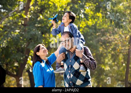 Nonna con ragazzo che tiene l'aeroplano giocattolo seduto sulla spalla del nonno al parco Foto Stock
