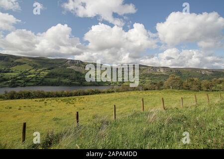 Estate con nuvole bianche e cielo blu in Irlanda rurale con una vista oltre la recinzione in filo e i campi verdi attraverso il lago Glencar per le montagne Dartry. Foto Stock