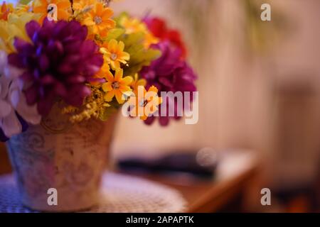 Un bouquet lussureggiante di fiori artificiali in un vaso di fiori si erge su un tavolo nel soggiorno. Foto Stock