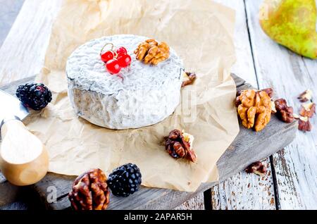 Diversi tipi di formaggi Deliziosi su una tavola di legno e molti snack, noci, miele, bacche, olive su un vecchio tavolo di legno bianco. Gli ingredienti del cibo sono tornati Foto Stock