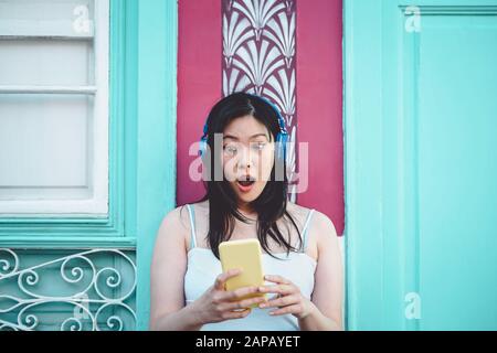 Felice ragazza asiatica l'ascolto di musica con cuffie per esterni - una giovane donna cinese giocando la sua playlist preferita la musica dal suo smartphone mobile app Foto Stock