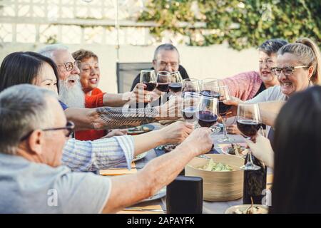 Buona famiglia che si rallegrano con il vino rosso a cena riunione in giardino - Senior divertirsi tostare gli occhiali da vista e mangiare insieme all'aperto Foto Stock