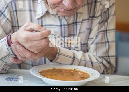 L'uomo anziano con malattia di Parkinsons tiene il cucchiaio in entrambe le mani. Foto Stock