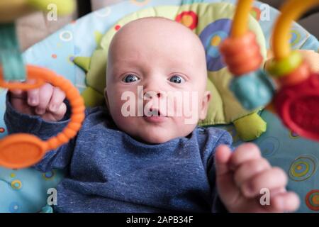 L'immagine quotidiana di stile di vita di un bambino carino età cinque mesi in una sedia di attività che guarda eccitato a giocattoli appesi interessanti. Inghilterra, Regno Unito, Gran Bretagna Foto Stock