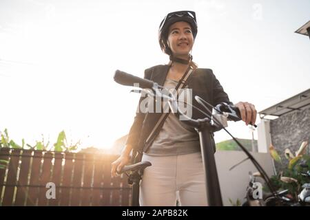 donna asiatica che indossa casco e borsa prepara una bicicletta pieghevole da casa per andare al lavoro Foto Stock