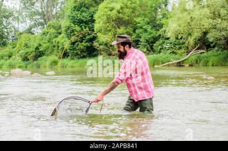 Se peschi regolarmente sapete quanto la pesca gratificante e lenitiva è. Hobby di pesca. Pesce di trota pescatino brutale barbuto con rete. La pesca è uno straordinario sport ricreativo all'aperto accessibile con sedia a rotelle. Foto Stock