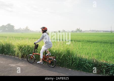Le donne asiatiche indossano i caschi per guidare le bici pieghevoli nei campi di riso Foto Stock