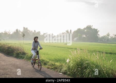 le giovani donne indossano i caschi per guidare le biciclette pieghevoli in risaie di fondo Foto Stock