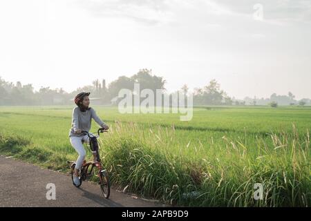 Le donne asiatiche indossano i caschi per guidare le bici pieghevoli nei campi di riso Foto Stock