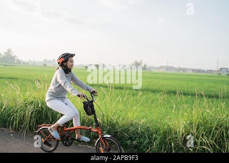 le giovani donne indossano i caschi per guidare le biciclette pieghevoli in risaie di fondo Foto Stock