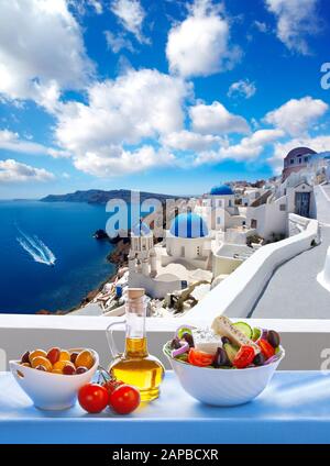 Insalata greca contro la famosa chiesa nel villaggio di Oia - Santorini Island in Grecia Foto Stock