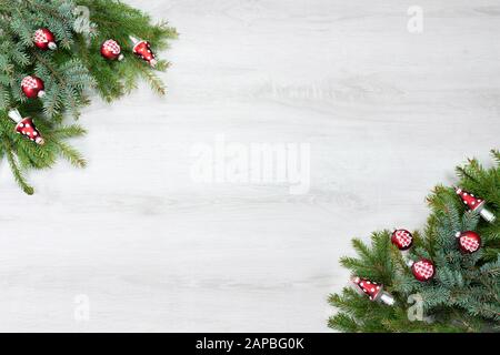 Rami di abete rosso e rami di abete sono in 2 angoli. Rosso albero di Natale ornamento come palle e fungo. Sfondo in legno bianco con spazio per il de personalizzato Foto Stock