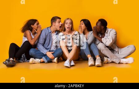 La ragazza scioccata che ascolta i suoi compagni di classe sussurra Foto Stock