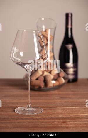 Vetro lucido cristallo, bottiglia di vino rosso, decanter trasparente riempito con tappi su tavolo di legno. Primo piano, verticale, messa a fuoco selettiva, vista laterale Foto Stock