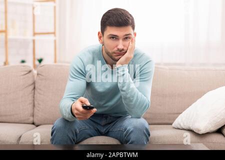 Guy Annoiato Cambio Canali Guardare La Tv Seduto Sul Divano Interno Foto Stock