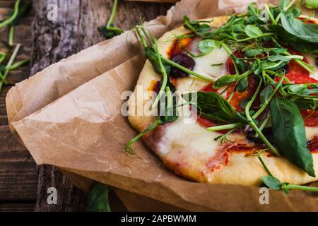 Pizza margarita fresca fatta in casa con pomodoro, verde e basilico su una tavola di legno rurale in carta artigianale, da vicino Foto Stock