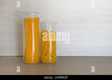 Pasta in vasi di vetro grandi contenitori stand su tavolo grigio in cucina. Pasta italiana cruda crudo con spaghetti. Foto Stock