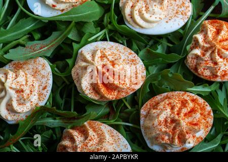 Uova divorate con paprika su insalata di rucola fresca in piatto rurale nero su tavola di legno, sano antipasto vegetariano o spuntino vicino Foto Stock