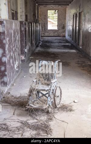 Una sedia a rotelle coperta di polvere nel corridoio abbandonato di un edificio abbandonato, spazio copia, nessuna gente Foto Stock