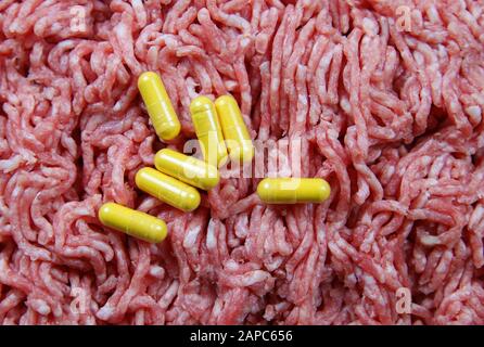 Uso di antibiotici negli animali da produzione alimentare concetto: Capsule gialle con fondo di carne cruda macinata Foto Stock