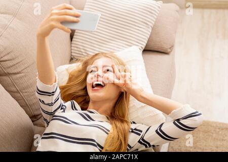 Felice ragazza che prende selfie mentre si trova sul divano Foto Stock